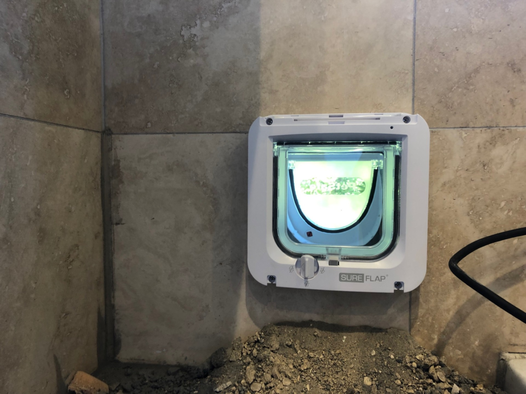  SureFlap microchip-activated cat flap  fitted in a beige-marble effect tiled wall. Before cleaned up.