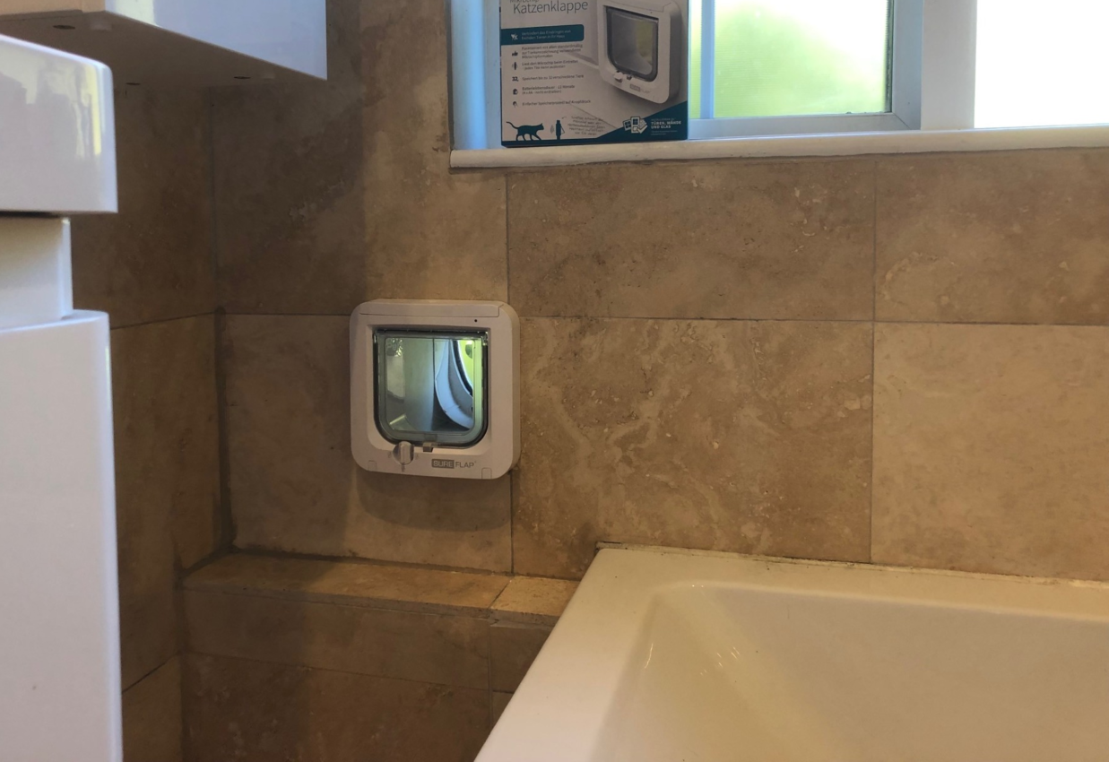SureFlap microchip-activated cat flap  fitted in a beige-marble effect tiled wall. The cat flap box sits on a window sill above