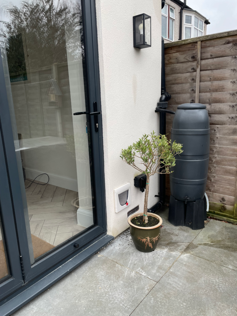  Outside view of a standard PetSafe cat flap in a white rendered wall. next to a grey bio-fold door